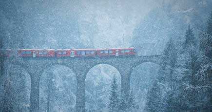 スイスの列車が雪の降る築100年の橋を通る　童話の世界のよう